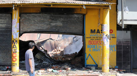 A man walks past damaged shops after overnight unrest and looting in Alexandra township, Johannesburg, South Africa © Reuters / Marius Bosch