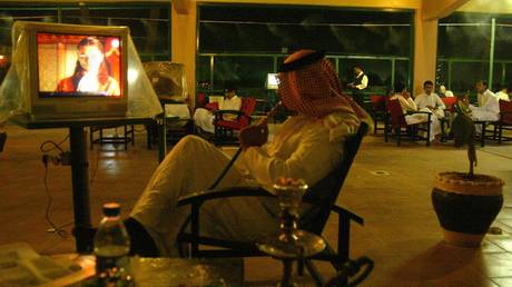 A Saudi citizen smokes a hookah (traditional waterpipe) while watching TV at a cafe in Riyadh