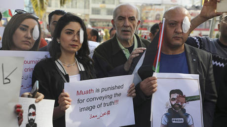 Palestinian journalists hold posters and wear eye patches as they rally in the West Bank city of Nablus on November 17, 2019.