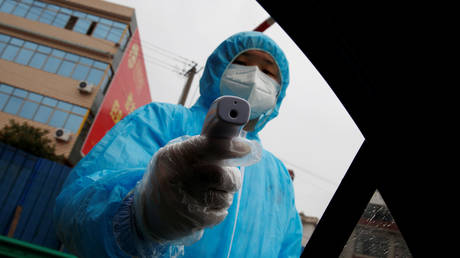 A medical worker holds a thermometer to check a passenger's temperature at a checkpoint in China as the country is hit by an outbreak of a lethal coronavirus, February 6, 2020.