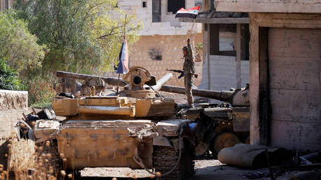 FILE PHOTO. A Syrian army soldier holds a Syrian flag as he stands on a military vehicle in Khan Sheikhoun, Idlib, Syria. ©REUTERS / Omar Sanadiki