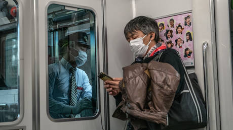 A train guard and passenger both wear face masks as they ride the Yamanote Line on March 27, 2020 in Tokyo, Japan