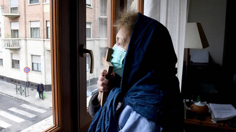 A woman wearing a protective face mask kisses a cross as she prays in her apartment in Turin, Italy, March 25, 2020 © Reuters / Massimo Pinca