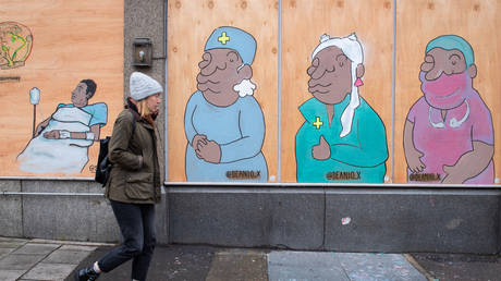 A woman passes a mural showing doctors and nurses in south London, as the UK continues in lockdown to help curb the spread of coronavirus